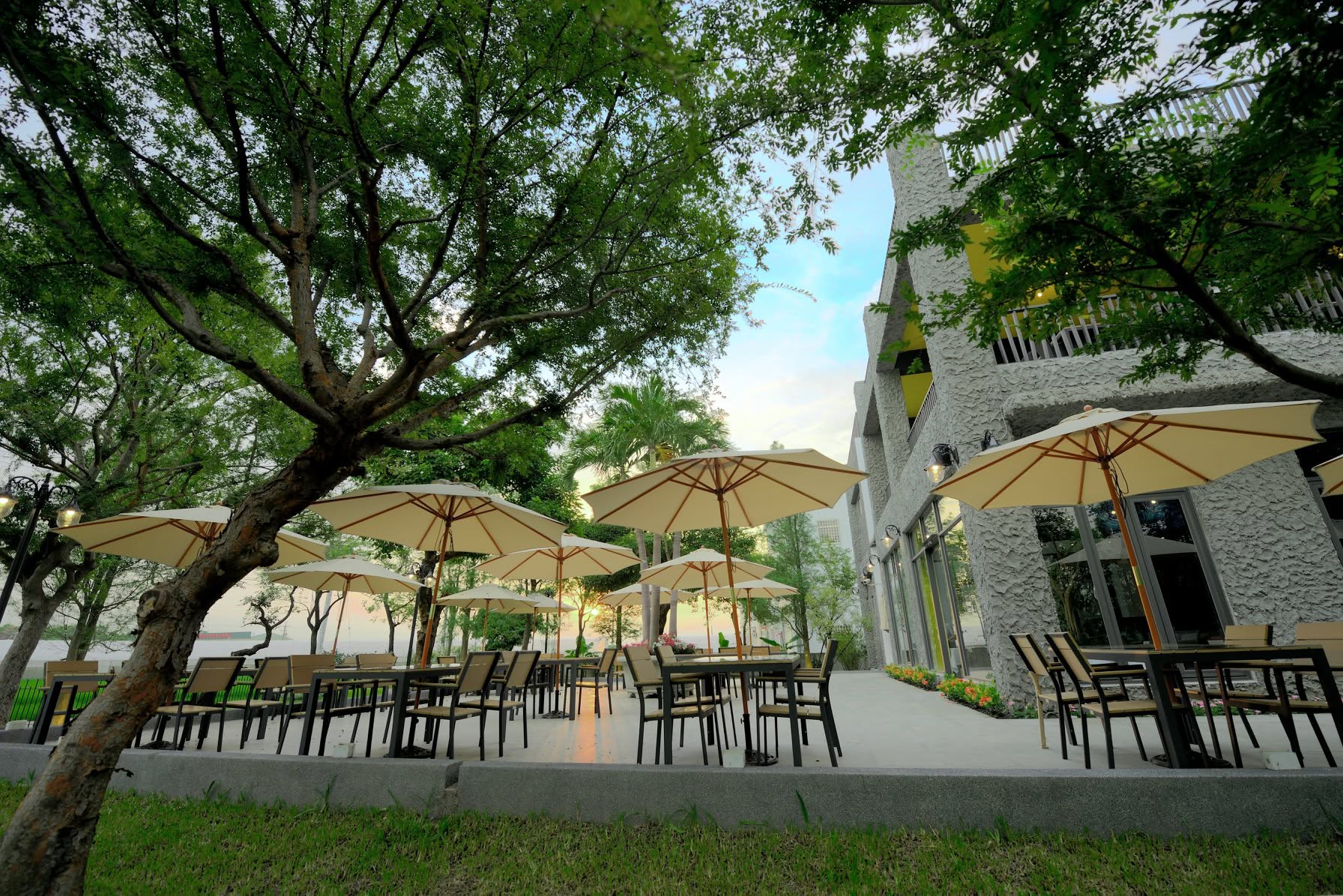 家園戶外用餐區，大樹樹蔭、陽傘與餐桌，旁邊為餐廳建築